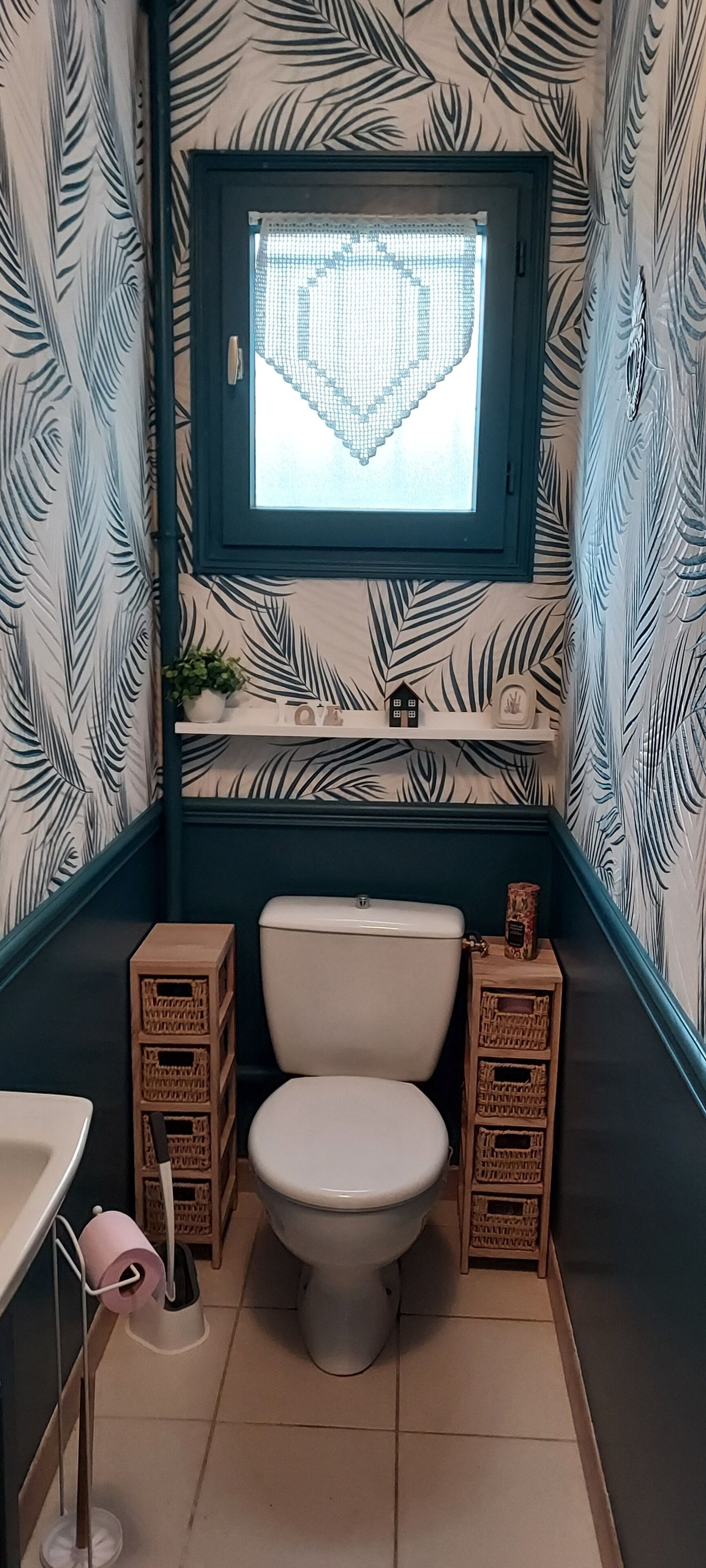 Ein Badezimmer mit Toilette, einem Fenster und gemustertem Tapeten.