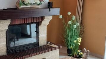 Een woonkamer met een open haard, een flatscreentelevisie aan de muur, een ronde houten tafel met metalen poten en een bloeiende plant in pot.