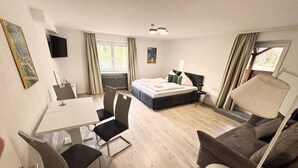 Una habitación de hotel con cama, escritorio con silla, sofá, televisor montado en la pared y ventana con cortinas.