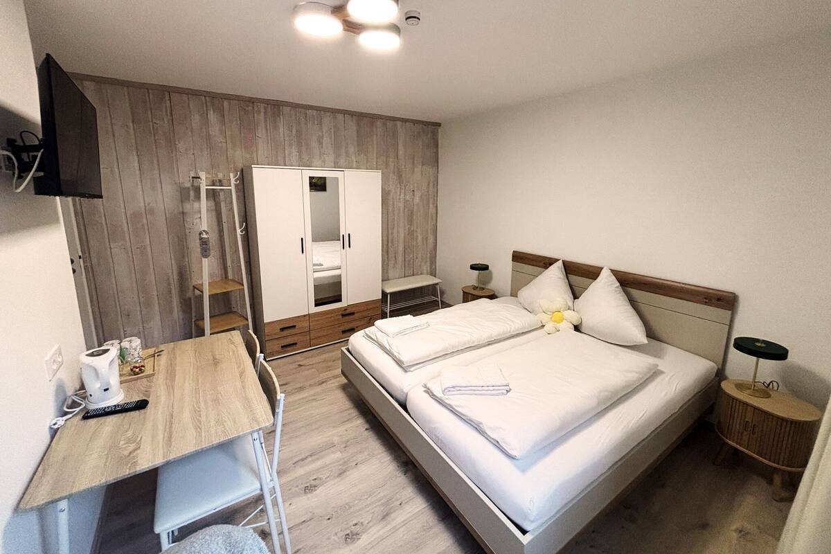 A bedroom with a bed, a desk, a wardrobe, and a mirror.