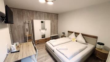 A bedroom with a bed, a desk, a wardrobe, and a mirror.