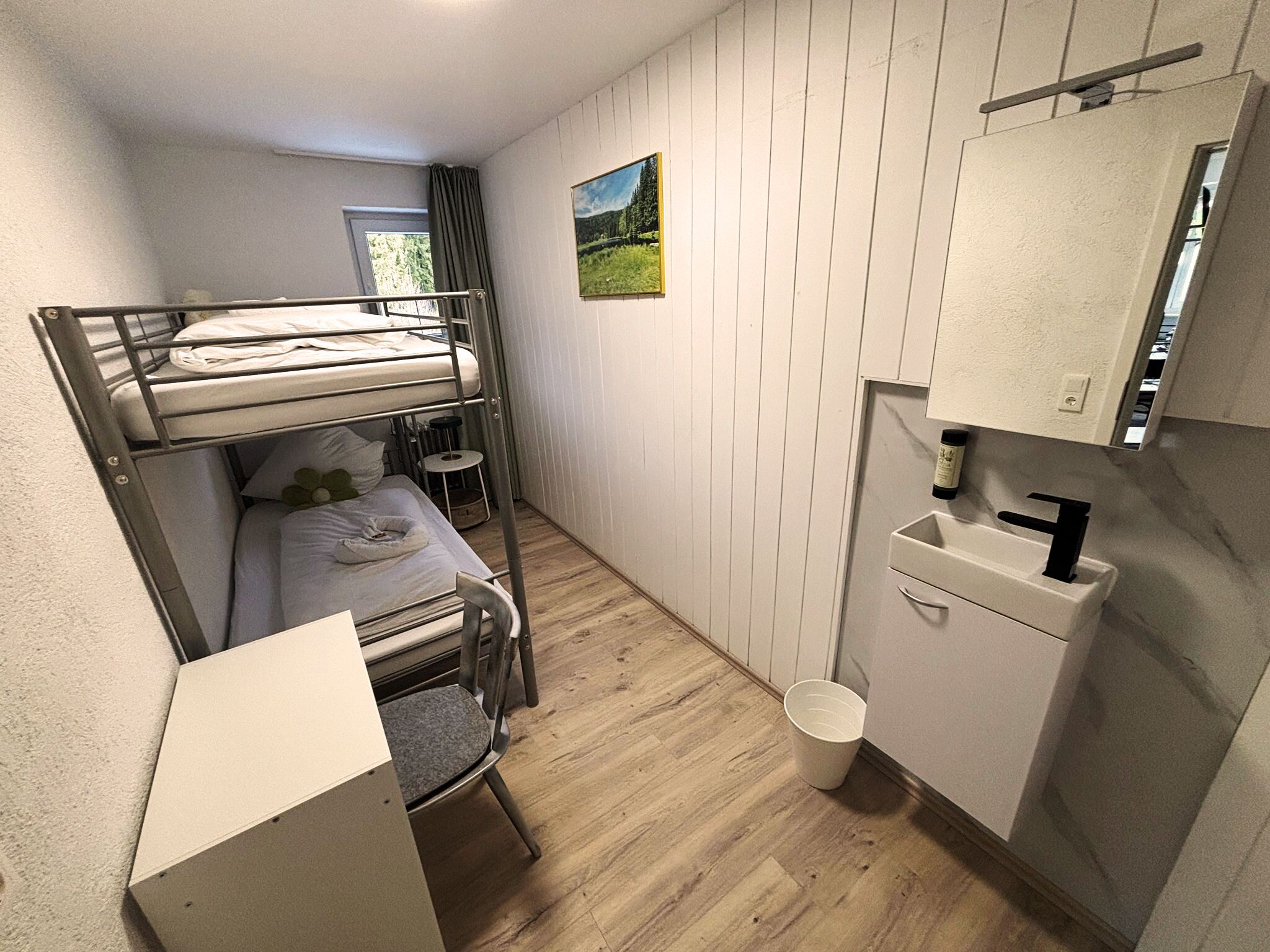Ein kleines Zimmer mit Etagenbetten, einem kleinen Schreibtisch, einem Stuhl, einem Waschbecken und einem Fenster.