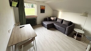 Una habitación con un sofá modular, una mesita, un radiador, un televisor, una lámpara y una ventana con cortinas.