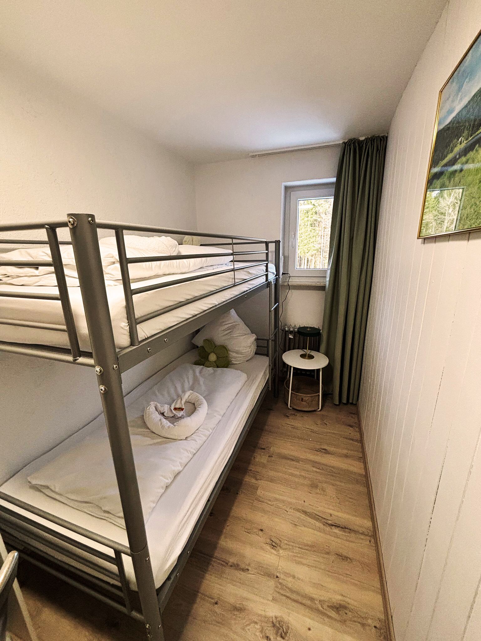 Kerrossängyllä varustettu huone, jossa on pieni pöytä ja ikkuna, jossa on verhot.