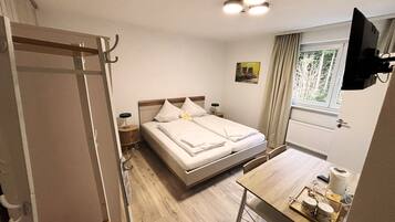 A bedroom with a bed, bedside tables, a desk, a chair, and a window.