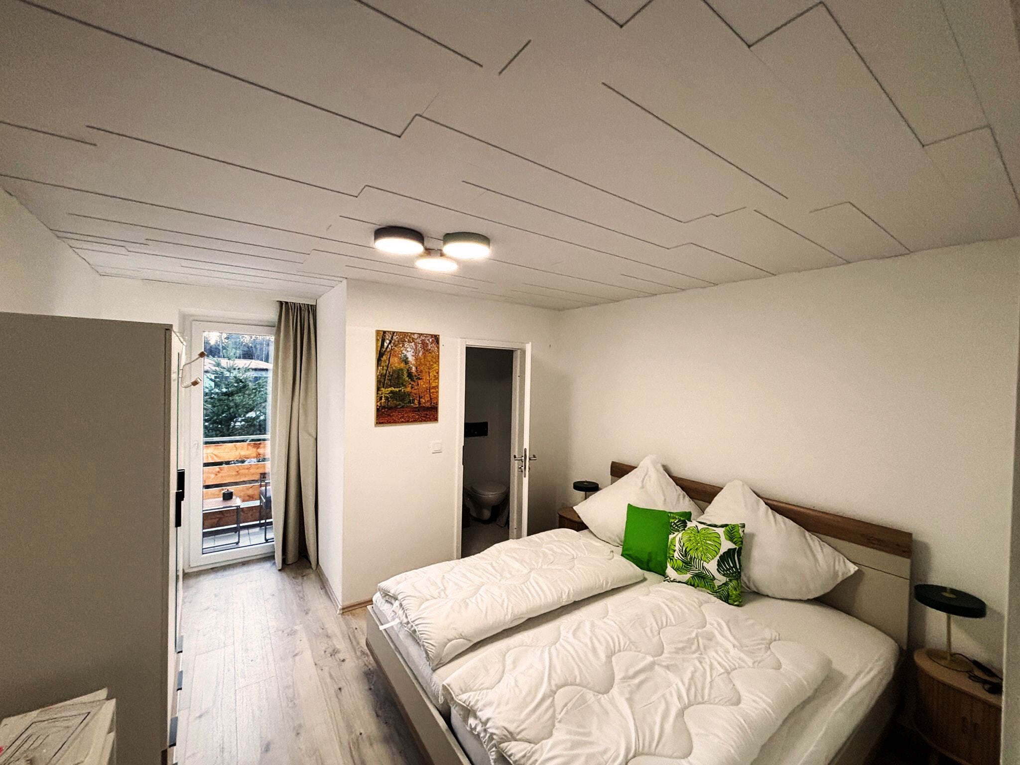 Ein Schlafzimmer mit einem Bett, einem Nachttisch, einem Fenster mit Vorhängen, einer Tür und einem Bild an der Wand.