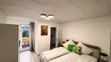 Ein Schlafzimmer mit einem Bett, einem Nachttisch, einem Fenster mit Vorhängen, einer Tür und einem Bild an der Wand.