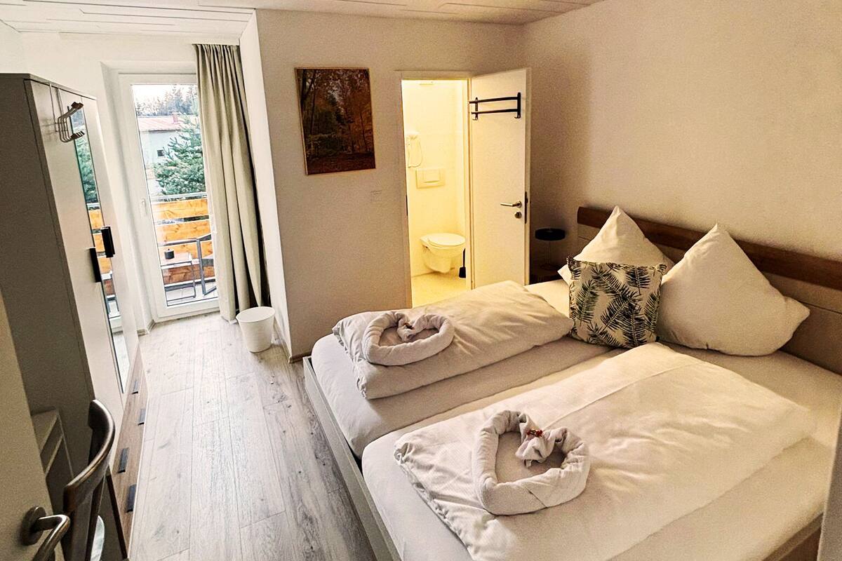 A hotel room with a bed, a bathroom, a door leading to a balcony, and a ceiling light fixture.