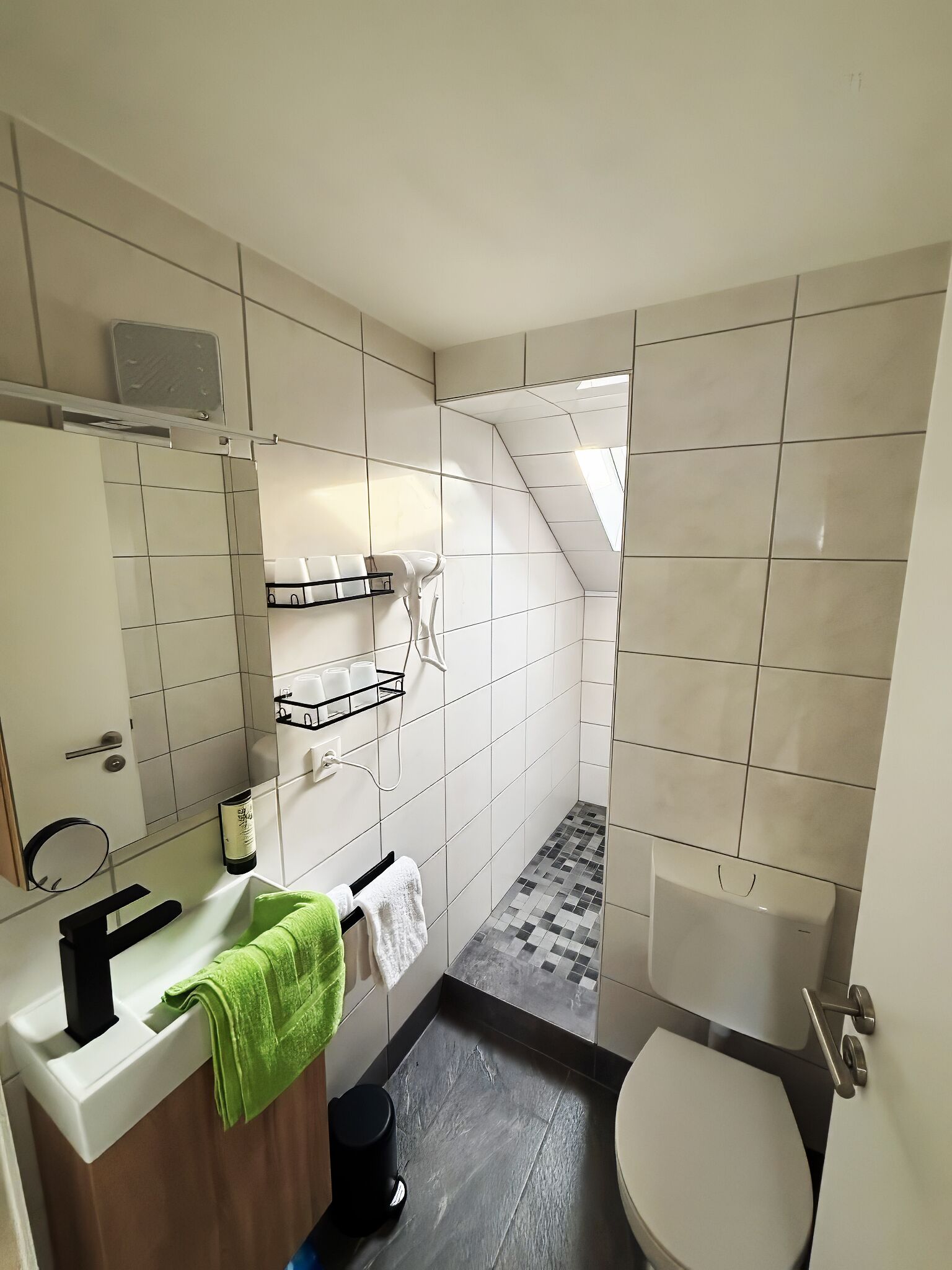 A small, modern bathroom with a shower, toilet, and sink.