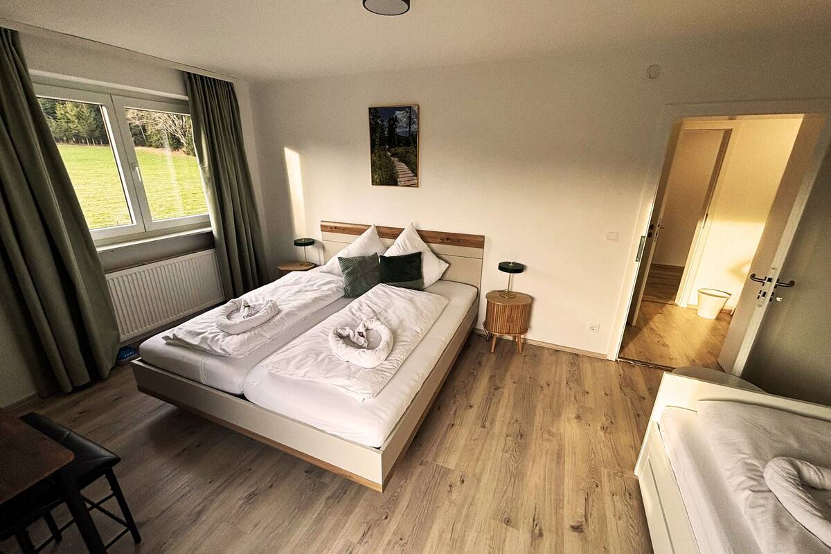 A room with a bed, a desk, and a view of a grassy area outside.