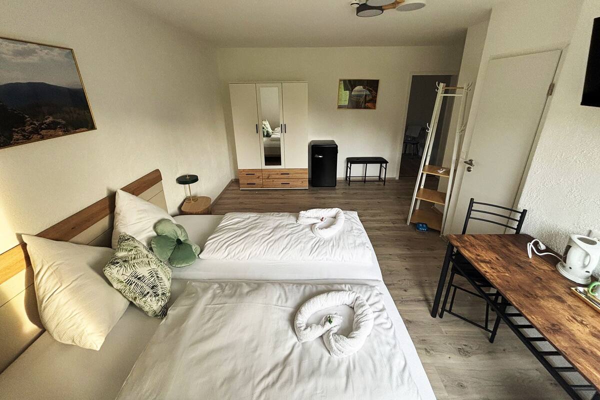 A hotel room with a bed, bedside table, chair, and a view of the hallway.