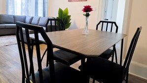 A dining area with a table, chairs, a vase with flowers, a sofa, and a plant.