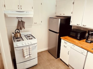 A compact kitchen with a gas stove, a refrigerator, a microwave, and a dishwasher.