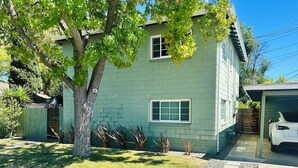 A two-story house with a green exterior, a driveway, a tree, and a white car parked in the garage. - Charming & Bright 1-bedroom w/private laundry & yard in Sacramento (Sacramento)
