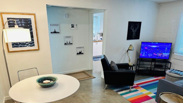 A modern living room with a round table, a black sofa, a colorful rug, a TV, and city-themed wall art. - Charming & Bright 1-bedroom w/private laundry & yard in Sacramento (Sacramento)