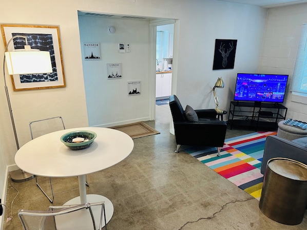 A modern living room with a round table, a black sofa, a colorful rug, a TV, and city-themed wall art.