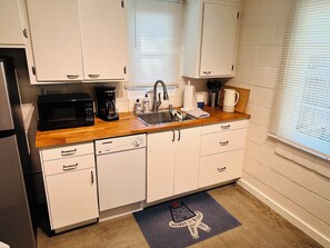 A kitchen with white cabinets, a microwave, a coffee maker, a sink, and a window with blinds.