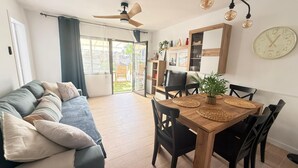 Una sala de estar moderna con un sofá, una mesa de comedor, sillas, un ventilador de techo y un reloj grande en la pared.