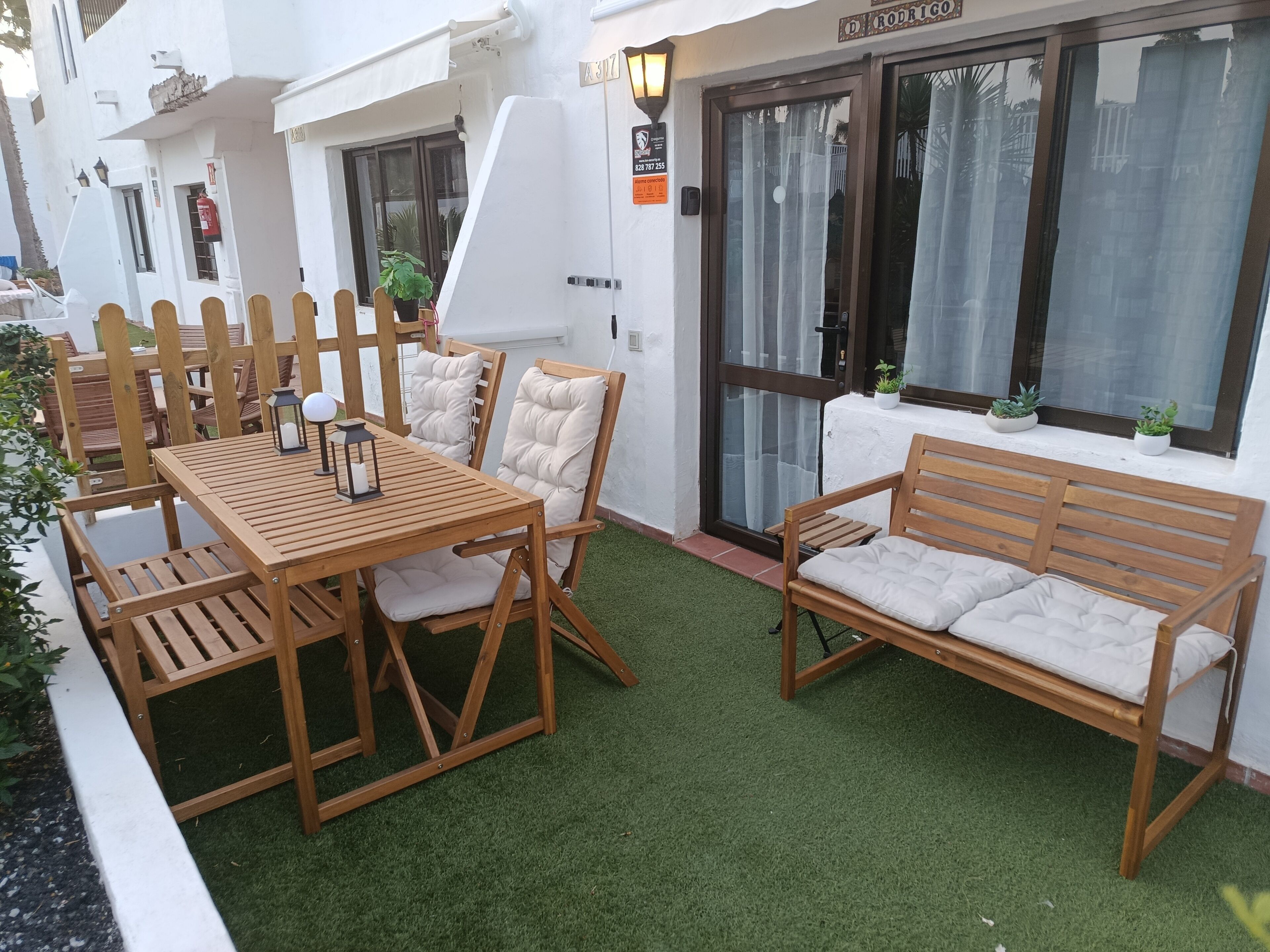 A patio with a wooden table and chairs, a wooden bench, and a small potted plant.