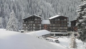 Um hotel de vários andares com varandas, rodeado por árvores cobertas de neve e uma paisagem montanhosa.