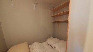Quarto pequeno com cama de solteiro, cabeceira de madeira, roupa de cama branca e prateleira embutida sobre a cama.