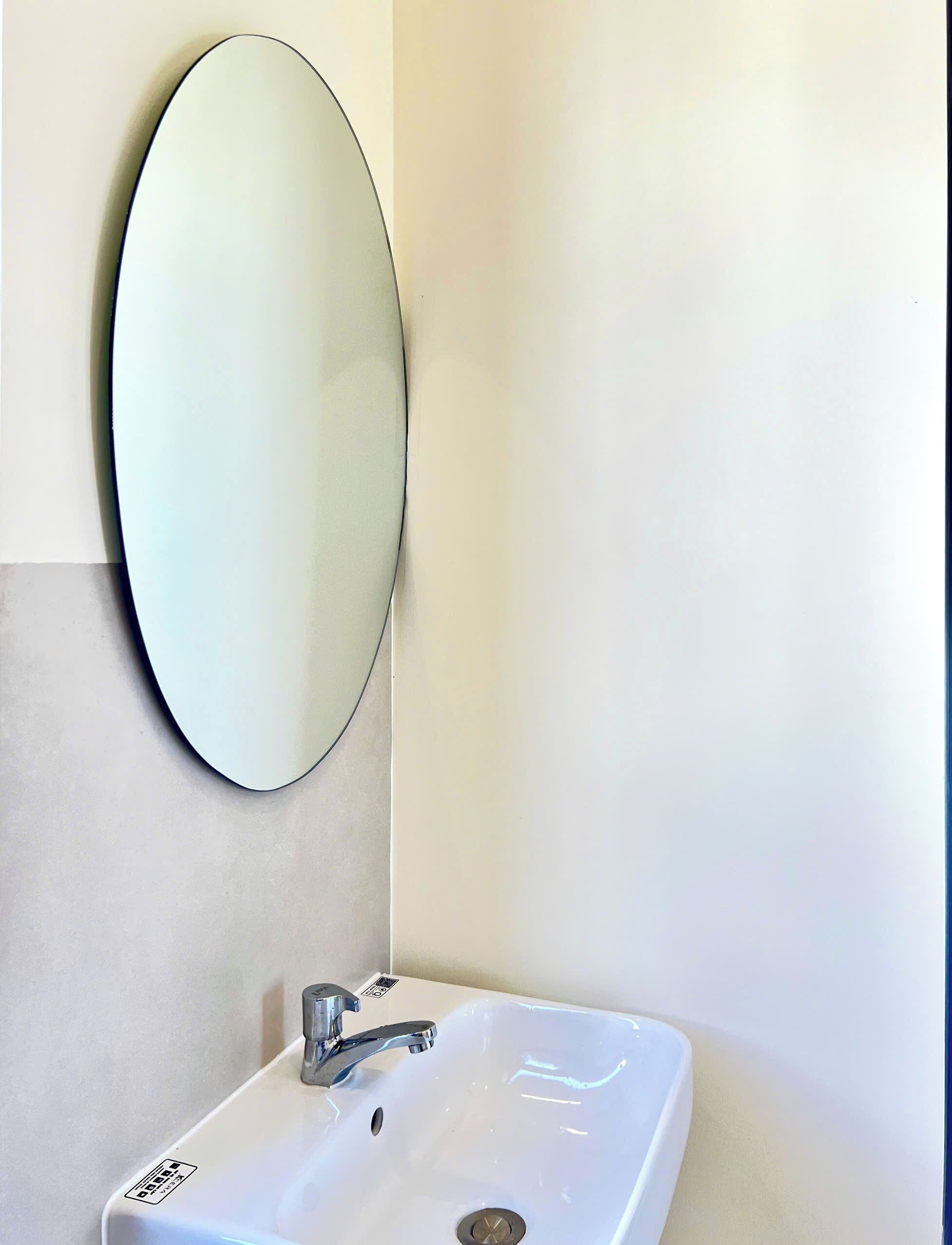 A bathroom with a white sink, a chrome faucet, and a wall-mounted oval mirror.