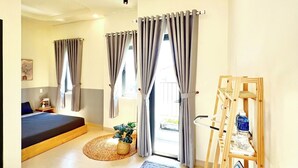 Une chambre moderne avec un lit, une petite table agrémentée d’une plante, une étagère en bois avec des serviettes et une vue sur l’extérieur.