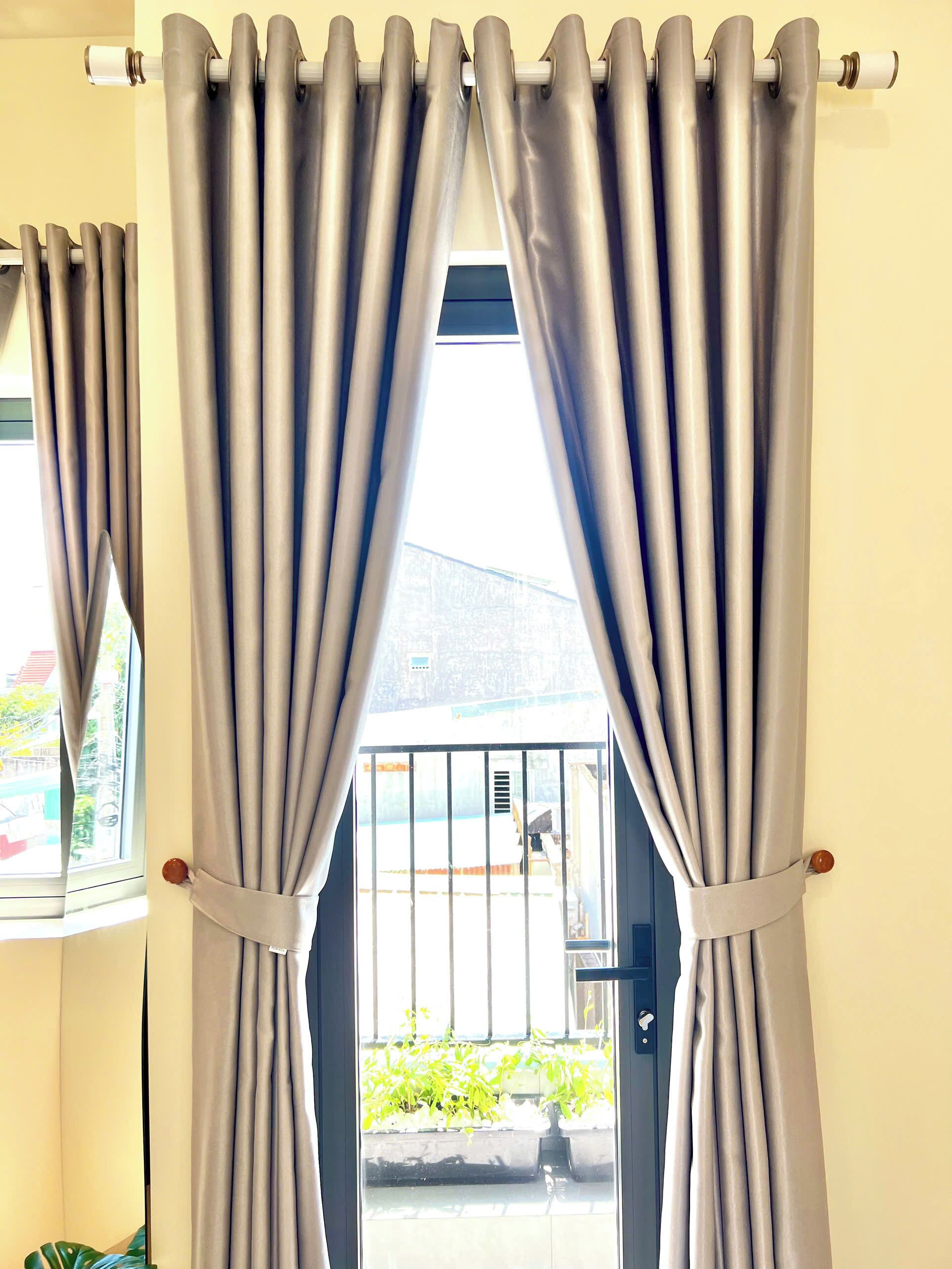 A room with a view through a window with curtains, a door with a metal gate, and a plant outside.
