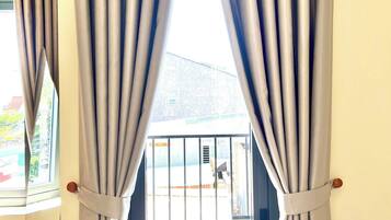 A room with a view through a window with curtains, a door with a metal gate, and a plant outside.