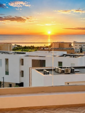 A rooftop with air conditioning units, a view of the sea, and buildings in the background.