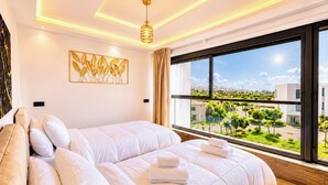 Une chambre d’hôtel moderne avec un grand lit, une vue sur un paysage verdoyant et un plafond doté d’un éclairage encastré.