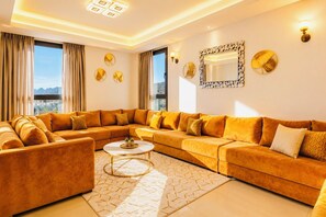 A modern living room with a large sectional sofa, a round coffee table, and a city view through large windows.