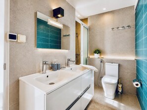 Un baño moderno con un lavamanos doble, inodoro, ducha y espejo con lámpara arriba.