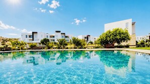 Une piscine à l’eau d’un bleu cristallin, entourée de bâtiments modernes et de verdure.