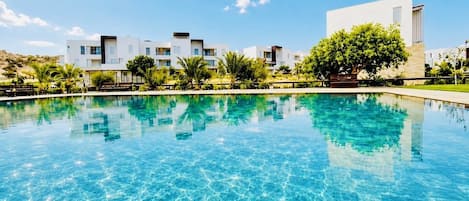 A swimming pool with clear blue water, surrounded by modern buildings and greenery.