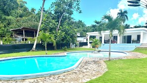 A swimming pool with a stone border, surrounded by grass and palm trees. - Villa with lagoon pool 10 minutes from the center (El Limón)
