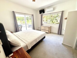 A bedroom with a bed, a TV, a dresser, and a window with curtains.