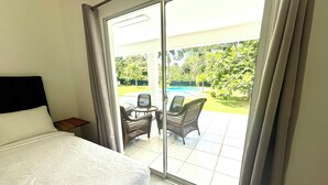 A hotel room with a bed, a small table, wicker chairs, and a view of a swimming pool and garden. - Villa with lagoon pool 10 minutes from the center (El Limón)