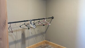Una habitación con piso de madera, un perchero metálico con ropa y una pared lisa.