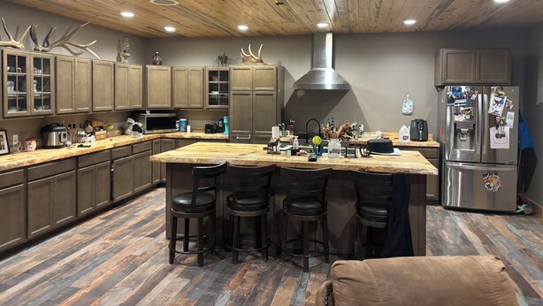 Una cocina moderna con armarios de madera, una isla central con taburetes, electrodomésticos de acero inoxidable y una campana extractora grande.