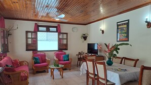 A cozy living room with wooden ceiling, a dining area with a table and chairs, a television, and a clock on the wall. - Stay at Villa Désiré, located in Le Vauclin, south of Martinique. (Le VAUCLIN)