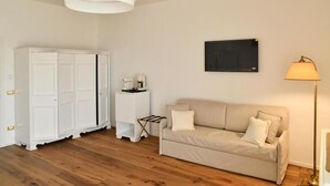 A room with a wooden floor, a beige sofa, a white wardrobe, a small table with a lamp, and a wall-mounted picture. - Casa FEREMI (Cavallino)