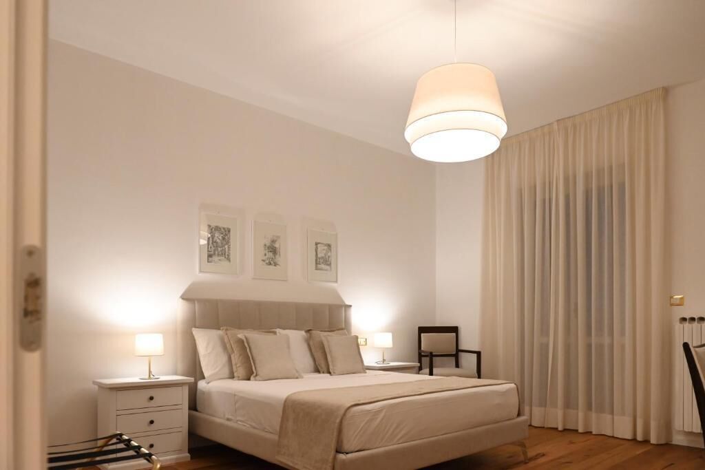 Une chambre à coucher avec un lit, des tables de chevet, une chaise et une grande fenêtre avec des rideaux.