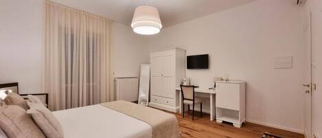 A hotel room with a bed, a desk, a chair, a TV, and a wardrobe.