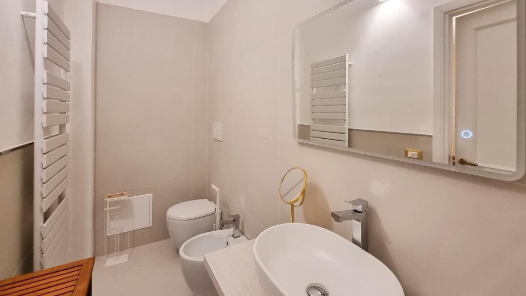 A bathroom with a toilet, bidet, sink, mirror, and towel rack.