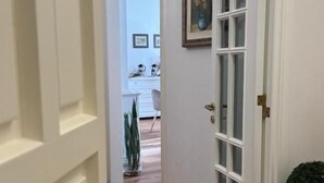 A hallway with a wooden floor, a white door with a glass panel, and a potted plant. - Casa FEREMI (Cavallino)