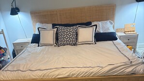 A bed with a woven headboard, a bedside table with a lamp, and a digital clock. - CONDO 2 BEDRM, EXPANSIVE PRIVATE DECK! WALKABLE to all HOT SPOTS w/ POOL (Margate City)