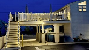 A building with a balcony, stairs, and a covered area with a trash bin. - CONDO 2 BEDRM, EXPANSIVE PRIVATE DECK! WALKABLE to all HOT SPOTS w/ POOL (Margate City)