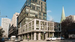 A multi-story building with large windows, a corner entrance, and a green spire in the background. - Modern Urban Retreat with Skyline Panorama (Montreal)