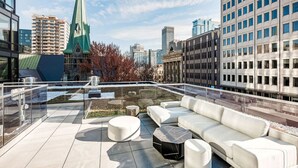 A rooftop terrace with a modern seating area, a view of a cityscape, and a distinctive green building in the background. - Modern Urban Retreat with Skyline Panorama (Montreal)